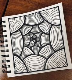 a spiral notebook with black and white drawing on it, sitting next to a pen