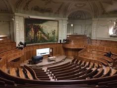 an empty auditorium filled with lots of wooden seats next to a painting on the wall