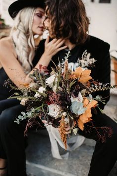 two people sitting on a bench with flowers in their hands and one person kissing the other