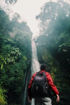 a man with a backpack is standing in front of a waterfall and looking up into the sky