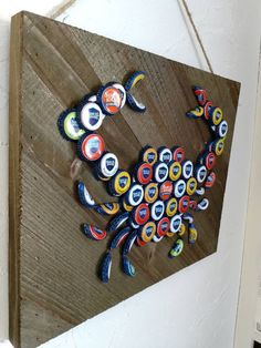 a crab made out of beer bottle caps on a wooden board hanging from the wall