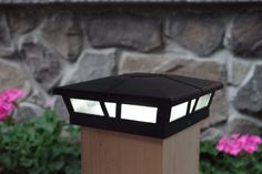 a light that is sitting on top of a wooden post in front of some flowers