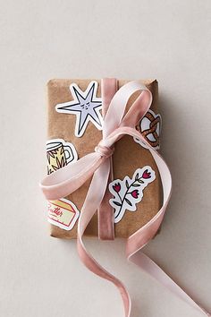 a present wrapped in brown paper with pink ribbon and stickers on it's side