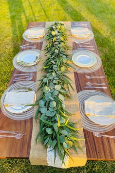 a long table with plates and greenery on it