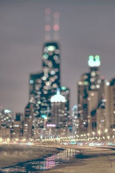 the city skyline is lit up at night with lights reflecting in the water on the beach