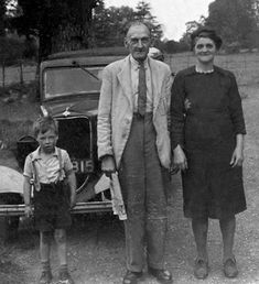 an old black and white photo of two adults and a child standing in front of a car