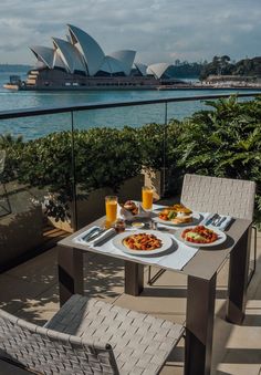 two plates of food are sitting on a table outside near the water and an opera