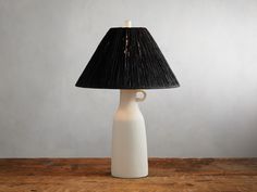 a table lamp with a black shade on it and a white vase in the middle