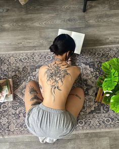 a woman is sitting on the floor with her back to the camera and tattoos on her body