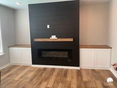 an empty room with wood floors and a black fireplace in the center, along with white paneling on the walls