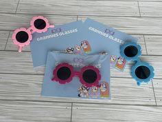 two pink and blue sunglasses sitting on top of a wooden floor next to each other