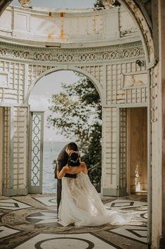 a bride and groom kissing in an archway at the end of their wedding day by the water