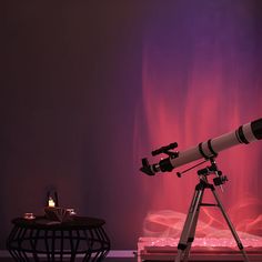 a telescope sitting on top of a tripod next to a table with a candle