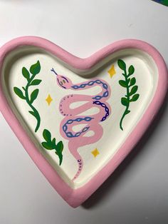 a pink heart shaped dish with a snake painted on it