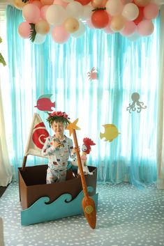 a little boy is sitting in a boat with balloons on the ceiling and holding a paddle