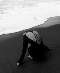 a woman sitting on top of a sandy beach next to the ocean with waves coming in