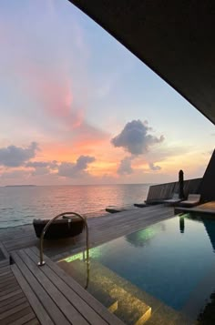 a wooden deck next to a swimming pool at sunset with the ocean in the background