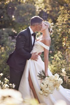 a bride and groom kissing in the middle of some bushes with white flowers on it