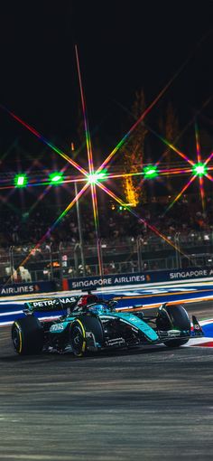 a racing car driving down a race track at night with bright lights in the background