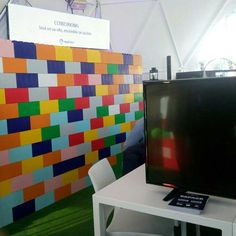 a television sitting on top of a white table next to a wall covered in lego blocks