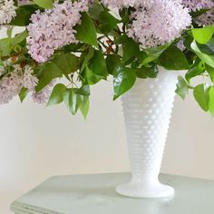 a white vase filled with purple flowers sitting on top of a green table next to a stack of books