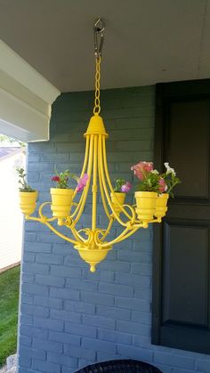 a yellow chandelier with flowers hanging from it's sides on a porch