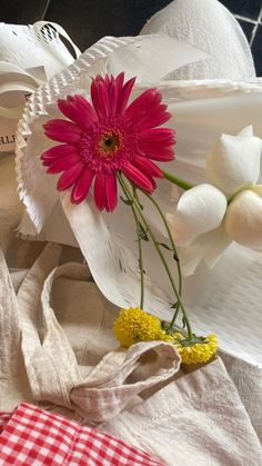 a pink flower sitting on top of a white plate next to a red and white checkered bag