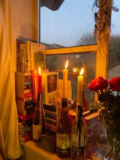 candles are lit on a window sill with books and wine bottles