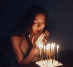 a girl blowing out candles on a cake with her hands in front of her face