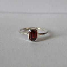 Wir stellen vor: unseren exquisiten Mini Granat Silberring, eine wahre Verkörperung von Eleganz und Raffinesse. Dieses hypnotisierende Stück zeichnet sich durch einen fesselnden roten Stein aus, der zart auf einem makellosen weißen Blatt thront, was einen auffälligen Kontrast schafft, der sicher ins Auge fällt. Dieser Granat Rechteck Ring wurde mit viel Liebe zum Detail gefertigt und verfügt über ein elegantes und zeitloses Design, das ihn zu einer idealen Wahl für jeden Anlass macht. Ob es ein Gold Unique Jewelry, Silver Red Ring, Garnet Silver Ring, Minimalist Sterling Silver Crystal Ring For Formal Occasions, Elegant Sterling Silver Stackable Ruby Ring, Gemstone Stackable Rings, Baguette Cut As Gift, Gemstone Stackable Rings With Baguette Cut For Gift, Elegant Stackable Ruby Ring In Sterling Silver, Minimalist Birthstone Ring With Baguette Cut Gemstone