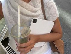 a woman holding a drink and cell phone in her hand while walking down the street