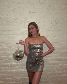 a woman in a silver dress holding a disco ball and pointing to the side with her finger