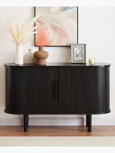 a black sideboard sitting on top of a wooden floor next to a white vase