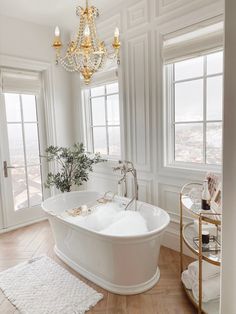 a large white bath tub sitting in a bathroom next to two windows and a chandelier