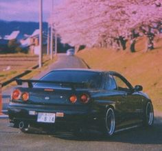 a black sports car parked on the side of the road with cherry blossoms in the background