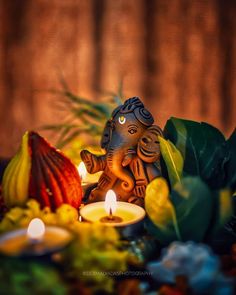 an elephant statue sitting on top of a table next to candles and flowers with leaves around it