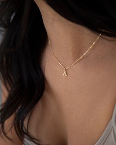 the back of a woman's neck wearing a gold necklace with an initial charm