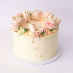 a white cake with pink flowers and macaroons on top, sitting on a plate