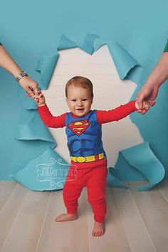 a little boy dressed as superman holding hands with his mother's hand in front of him