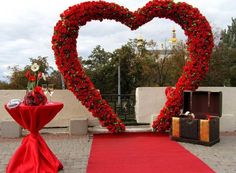 a heart shaped display with red flowers on the ground next to a table and suitcases