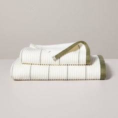 two white towels folded on top of each other, with green trimmings and an olive green cord