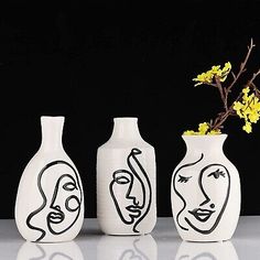 three vases with faces painted on them are next to a yellow flower and branch