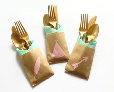 three gold forks and two brown paper bags with pink designs on them, sitting next to each other