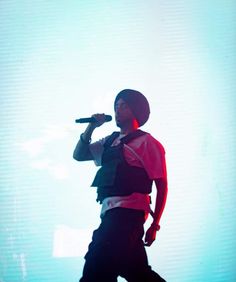 a man standing on top of a stage holding a microphone in his hand and wearing black pants