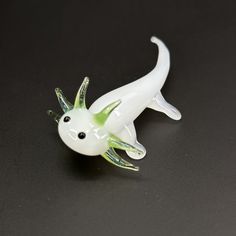 a white and green plastic toy lizard on a black surface with its mouth open to the side