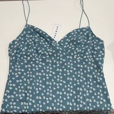 a blue top with white flowers on it and a tag hanging from the neckline