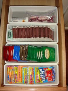 an open drawer with three containers filled with snacks and candy bar wrappers in it