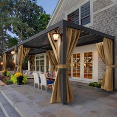 a patio covered in curtains and lights next to a house at night with outdoor dining area