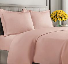 a bed with pink sheets and yellow flowers in a vase on the nightstand next to it