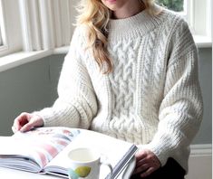 a woman sitting at a table with a book and coffee cup in front of her